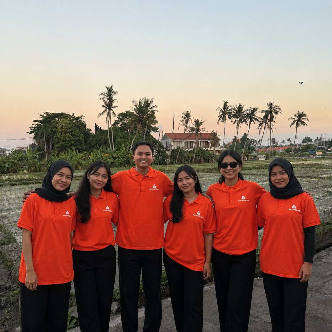 The NomadCare team in orange shirts, standing in front of Bali rice fields at sunset
